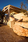 CORFU  GREECE: VILLA IN NORTH EAST CORFU. DESIGN BY ALITHEA JOHNS OF SKOPOS DESIGN AND RAHDY ELWAN. PATIO AND LARGE ROCK IN FRONT OF STEPS AND HOUSE