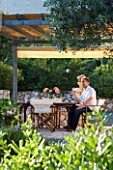 CORFU  GREECE. MALAMA HOUSE NEAR BARBATI. MAN (AGED 35) DRINKING A GLASS OF WINE AT A TABLE SET FOR ALFRESCO DINING BENEATH PERGOLA. PATIO  TABLE AND CHAIRS. RELAXED