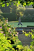 MARINERS GARDEN  BERKSHIRE. DESIGNER FENJA ANDERSON - VIEW INTO THE ROSE GARDEN TO THE WATER LILY POOL WITH HERON SCULPTURE. ROSE FANTIN LATOUR IN THE FOREGROUND