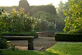 MARINERS GARDEN  BERKSHIRE. DESIGNER FENJA ANDERSON - VIEW INTO THE ROSE GARDEN AT DAWN TO THE WATER LILY POOL WITH HERON SCULPTURE.