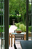 URBAN CONTEMPORARY MODERN MINIMALIST GARDEN DESIGNED BY CHARLOTTE SANDERSON: VIEW THROUGH KITCHEN DOOR TO PATIO WITH WOODEN TABLE AND CHAIRS AND PAVED PATH TO URN