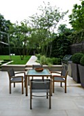 URBAN CONTEMPORARY MODERN MINIMALIST GARDEN DESIGNED BY CHARLOTTE SANDERSON: STONE PATIO WITH WOODEN TABLE AND CHAIRS AND PAVED PATH TO URN  LAWN