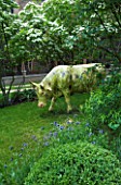 GARDEN DESIGNED BY CHARLOTTE SANDERSON: MODEL COW IN THE LAWN WITH CORNUS KOUSA BEHIND IN SPRING