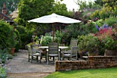 MARINERS GARDEN  BERKSHIRE. DESIGNER FENJA ANDERSON - PATIO WITH WINE AND RED BORDER AND UPPER BANK -  A PLACE TO SIT - TABLE AND CHAIRS AND CANOPY - PHYGELIUS  PENSTEMON FIREBIRD