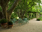 DESIGNER DOMINIQUE LAFOURCADE  PROVENCE  FRANCE - A PLACE TO SIT  GREEN CHAIRS AROUND A STONE TABLE WITH PERGOLA ND PLANE TREES. PATIO. TERRACE