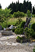 PROVENCE  FRANCE. GARDEN OF MARCO NUCERA. GRAVEL GARDEN WITH CLIPPED BOX  STONE WATER CONTAINER AND BEAUTIFUL WOODEN SCULPTED SEAT