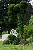 PROVENCE  FRANCE. GARDEN OF MARCO NUCERA. SCULPTED TREE WITH WATER FEATURE AND BEAUTIFUL WOODEN SCULPTURE BEHIND