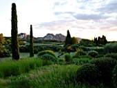 DESIGNER ALAIN DAVID IDOUX - MAS BENOIT  PROVENCE  FRANCE. VIEW TO MOUNTAINS WITH GRASSES AND CLIPPED CYPRESS TREES IN THE FOREGROUND. EVENING LIGHT