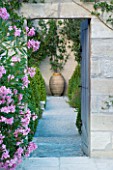 DESIGNER MICHEL SEMINI  PROVENCE  FRANCE. VIEW THROUGH DOORWAY PAST PINK OLEANDER ALONG PATH TO TERRACOTTA CONTAINER. FOCAL POINT