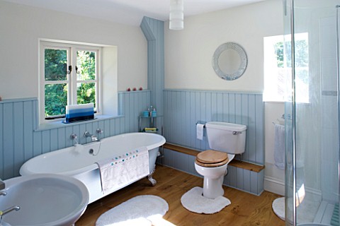 CLARE_MATTHEWS_HOUSE__DEVON_INTERIOR_OF_BATHROOM_WITH_ROLL_TOP_BATH__PALE_BLUE_WOOD_PANELLING_AND_WO