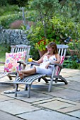 CLARE MATTHEWS GARDEN  DEVON. CLARE RELAXES WITH A DRINK IN A STEAMER CHAIR ON THE PATIO. A PLACE TO SIT  DECKCHAIR  RELAX  FUN