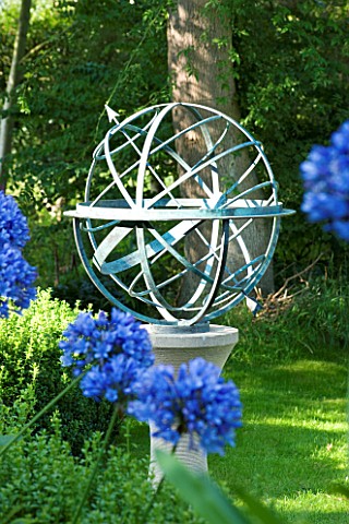 DAVID_HARBER_SUNDIALS_ARMILLARY_SPHERE_SUNDIAL_ON_STONE_PLINTH_WITH_AGAPANTHUS_IN_FOREGROUND