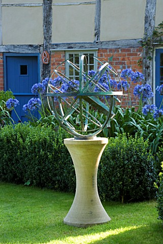 DAVID_HARBER_SUNDIALS_ARMILLARY_SPHERE_SUNDIAL_ON_STONE_PLINTH_WITH_AGAPANTHUS_IN_COTTAGE_FRONT_GARD