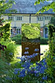 DAVID HARBER SUNDIALS: METAL TITAN SCULPTURE MADE FROM OXIDISED AND MIRROR-POLISHED STAINLESS STEEL WITH AGAPANTHUS IN FRONT GARDEN