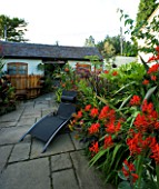 DARREN CLEMENTS GARDEN  STAFFORDSHIRE: BLACK SUN LOUNGER IN COURTYARD WITH CROCOSMIA LUCIFER  COTINUS GRACE AND HOT TUB IN BACKGROUND