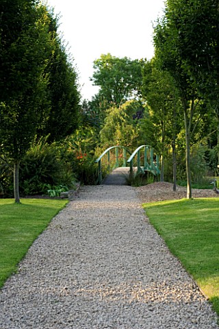 WILKINS_PLECK__STAFFORDSHIRE_A_GRAVEL_PATH_ALONG_A_LAWN_TO_A_BLUE_GIVERNY_TYPE_BRIDGE