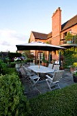WILKINS PLECK  STAFFORDSHIRE: VIEW FROM THE MAIN LAWN TO THE HOUSE WITH PATIO  WOODEN TABLE AND CHAIRS AND PARASOL/ UMBRELLA