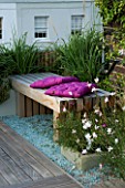 ROOF GARDEN  HOLLAND PARK  LONDON. DESIGNER: CHARLOTTE ROWE. WOODEN BENCH  MAUVE CUSHIONS ON DECKED TERRACE WITH PALE BLUE GLASS GRAVEL AND GAURA LINDHEIMERI WHIRLING BUTTERFLIES