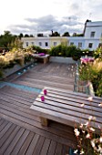 ROOF GARDEN  HOLLAND PARK  LONDON. DESIGNER: CHARLOTTE ROWE. WOODEN BENCH  CANDLES ON IPE DECKED TERRACE WITH BLUE GLASS GRAVEL  LED LIGHTING AND RAISED BEDS WITH GRASSES