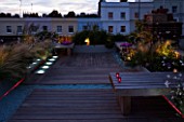 ROOF GARDEN  HOLLAND PARK  LONDON. DESIGNER: CHARLOTTE ROWE. DECKED TERRACE AT NIGHT WITH PINK & WHITE LED LIGHTING AND BLUE GLASS GRAVEL