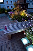 ROOF GARDEN  HOLLAND PARK  LONDON.DESIGNER:CHARLOTTE ROWE. DECKED TERRACE AT NIGHT WITH PINK & WHITE LED LIGHTING & WOODEN BENCH WITH CANDLES. RAISED BEDS WITH STIPA & GAURA