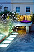 ROOF GARDEN  HOLLAND PARK  LONDON. DESIGNER: CHARLOTTE ROWE. DECKED TERRACE AT NIGHT WITH LED LIGHTING  STIPA TENUISSIMA  GAURA LINDHEIMERI WHIRLING BUTTERFLIES