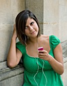 TEENAGE GIRL (16-17 YEARS) IN JEAN MINISKIRT AND GREEN TOP SITTING ON WALL LISTENING TO MP3 PLAYER. TEENAGE GIRLS  ONE TEENAGE GIRL ONLY  IPOD  MUSIC  CASUAL CLOTHING