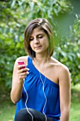 TEENAGE GIRL (16-17 YEARS) IN BLUE TOP SITTING LISTENING TO MP3 PLAYER. MUSIC  TEENAGE GIRLS  ONE TEENAGE GIRL ONLY  CASUAL CLOTHING  STUDENT  COLLEGE  MUSIC