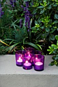 DESIGNER - CHARLOTTE ROWE  LONDON: CHARLOTTE ROWES OWN GARDEN AT NIGHT -  TEA LIGHTS (CANDLES) INSIDE PURPLE GLASS CONTAINERS BESIDE LIRIOPE MUSCARI