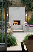 DESIGNER - CHARLOTTE ROWE  LONDON: CHARLOTTE ROWES OWN GARDEN AT NIGHT - VIEW OUT OF BACK DOOR ACROSS PORTUGUESE HONED LIMESTONE FLOORING  RENDERED RAISED BEDS AND FIREPLACE