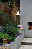 DESIGNER - CHARLOTTE ROWE  LONDON: CHARLOTTE ROWES OWN GARDEN AT NIGHT - RENDERED RAISED BED BESIDE FIREPLACE WITH LIRIOPE MUSCARI  MOROCCAN CANDLE HOLDER  CANDLES