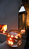 DESIGNER - CHARLOTTE ROWE  LONDON: CHARLOTTE ROWES OWN GARDEN AT NIGHT - LARGE GLASS BOWL WITH FLOATING CANDLES AND GERBERAS AND NICKEL PLATED BROMPTON LANTERN BESIDE FIREPLACE