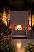 DESIGNER - CHARLOTTE ROWE  LONDON: CHARLOTTE ROWES OWN GARDEN AT NIGHT - PORTUGUESE HONED LIMESTONE FLOORING  RENDERED RAISED BEDS  PHILIPE STARCK CHAIRS AND OUTDOOR FIREPLACE
