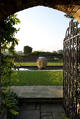 DAVID_HARBER_SUNDIALS_VIEW_THROUGH_A_GATE_AND_ARCHWAY_TO_ETHER_WATER_FEATURE_IN_A_POOL_IN_EARLY_MORN