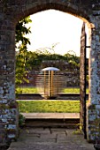 DAVID HARBER SUNDIALS: VIEW THROUGH A GATE AND ARCHWAY TO ETHER WATER FEATURE IN A POOL IN EARLY MORNING DAWN LIGHT WITH CHAMOMILE LAWN