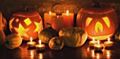 HALLOWEEN: STILL LIFE ON SIDEBOARD AT NIGHT WITH ORANGE CANDLES  PUMPKINS  SQUASHES AND GOURDS