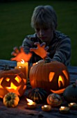 HALLOWEEN: BOY (AGED 13) PUTS HANDS UP TO CANDLE LIGHT - STILL LIFE ON WOODEN TABLE AT NIGHT WITH CANDLES  PUMPKINS  SQUASHES AND GOURDS
