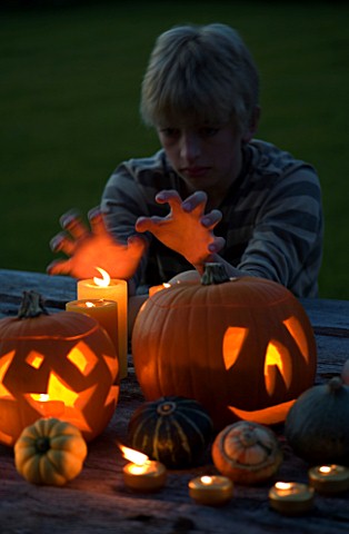 HALLOWEEN_BOY_AGED_13_PUTS_HANDS_UP_TO_CANDLE_LIGHT__STILL_LIFE_ON_WOODEN_TABLE_AT_NIGHT_WITH_CANDLE