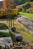 MARKS HALL  ESSEX : THE GARDEN OF SPHERES IN THE WALLED GARDEN: STONE BALLS  STONE STEPS AND AMELANCHIER X GRANDIFLORA ROBIN HILL