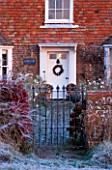 BOONSHILL FARM AT CHRISTMAS. VIEW OF THE FRONT OF THE HOUSE IN FROST WITH GATE AND COTONEASTER   WHITE DOOR AND WREATH. DESIGNER LISETTE PLEASANCE