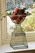 BOONSHILL FARM AT CHRISTMAS: WINDOW DECORATION - ORNATE METAL WIRE CONTAINERS WITH APPLES  IVY AND POMEGRANATES. DESIGNER: LISETTE PLEASANCE