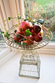 BOONSHILL FARM AT CHRISTMAS: WINDOW DECORATION - ORNATE METAL WIRE CONTAINERS WITH APPLES  IVY AND POMEGRANATES. DESIGNER: LISETTE PLEASANCE