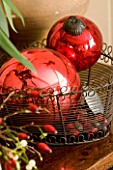 BOONSHILL FARM AT CHRISTMAS: DECORATIVE RED CHRISTMAS TREE BAUBLES IN A WIRE BASKET. DESIGNER: LISETTE PLEASANCE