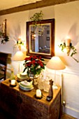 BOONSHILL FARM AT CHRISTMAS: THE DINING ROOM - LIGHTING - WALL CANDLES WRAPPED WITH IVY  MIRROR WITH MISTLETOE  SIDEBOARD WITH POINSETTIA IN CONTAINER. DESIGNER: LISETTE PLEASANCE