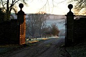 CERNEY HOUSE GARDEN  GLOUCESTERSHIRE: VIEW ALONG THE DRIVE TO THE FRONT GATE IN WINTER