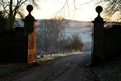 CERNEY_HOUSE_GARDEN__GLOUCESTERSHIRE_VIEW_ALONG_THE_DRIVE_TO_THE_FRONT_GATE_IN_WINTER