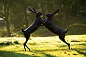 CERNEY HOUSE GARDEN  GLOUCESTERSHIRE: SCULPTURE OF BOXING HARES ON THE LAWN AT DAWN