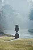JOHN MASSEYS GARDEN  WORCESTERSHIRE: WINTER - EARLY MORNING BACKLIGHTING ON AN URN ON THE LAWN BESIDE THE CANAL