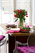 DESIGNER: CHARLOTTE ROWE  LONDON: THE DINING ROOM WITH TABLE WITH RED TULIPS IN A GLASS VASE  PINK NAPKINS AND FRESH STRAWBERRIES ON A PLATE