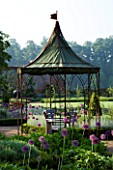 THE WALLED GARDEN AT COWDRAY  WEST SUSSEX. DESIGNER: JAN HOWARD - METAL GAZEBO WITH SEAT AND BOX EDGED BORDERS WITH ALLIUM PURPLE SENSATION